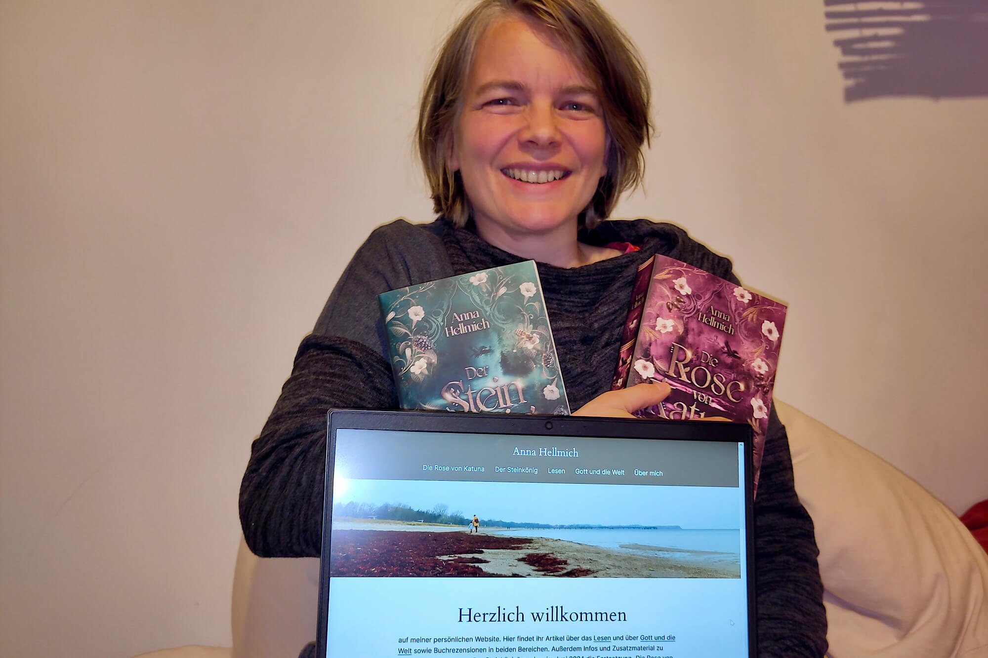 Anna Hellmich mit ihren Büchern und einem Laptop, auf dem ihre Website zu sehen ist