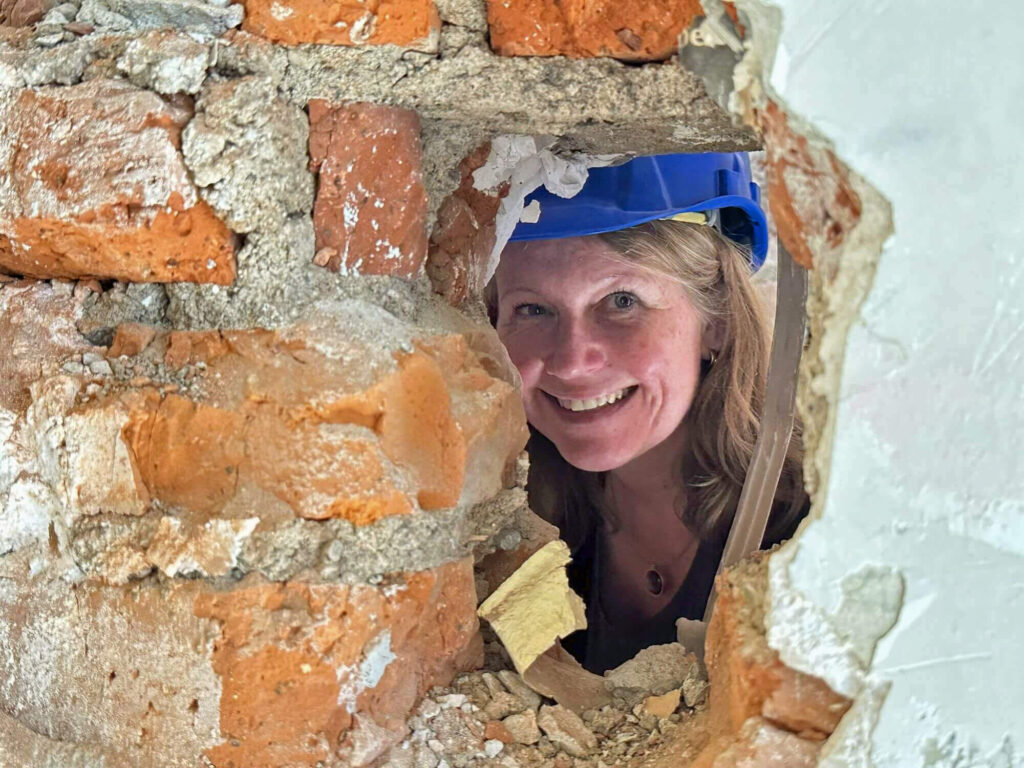 Architektin mit Helm schaut durch ein Loch in einer Ziegelwand